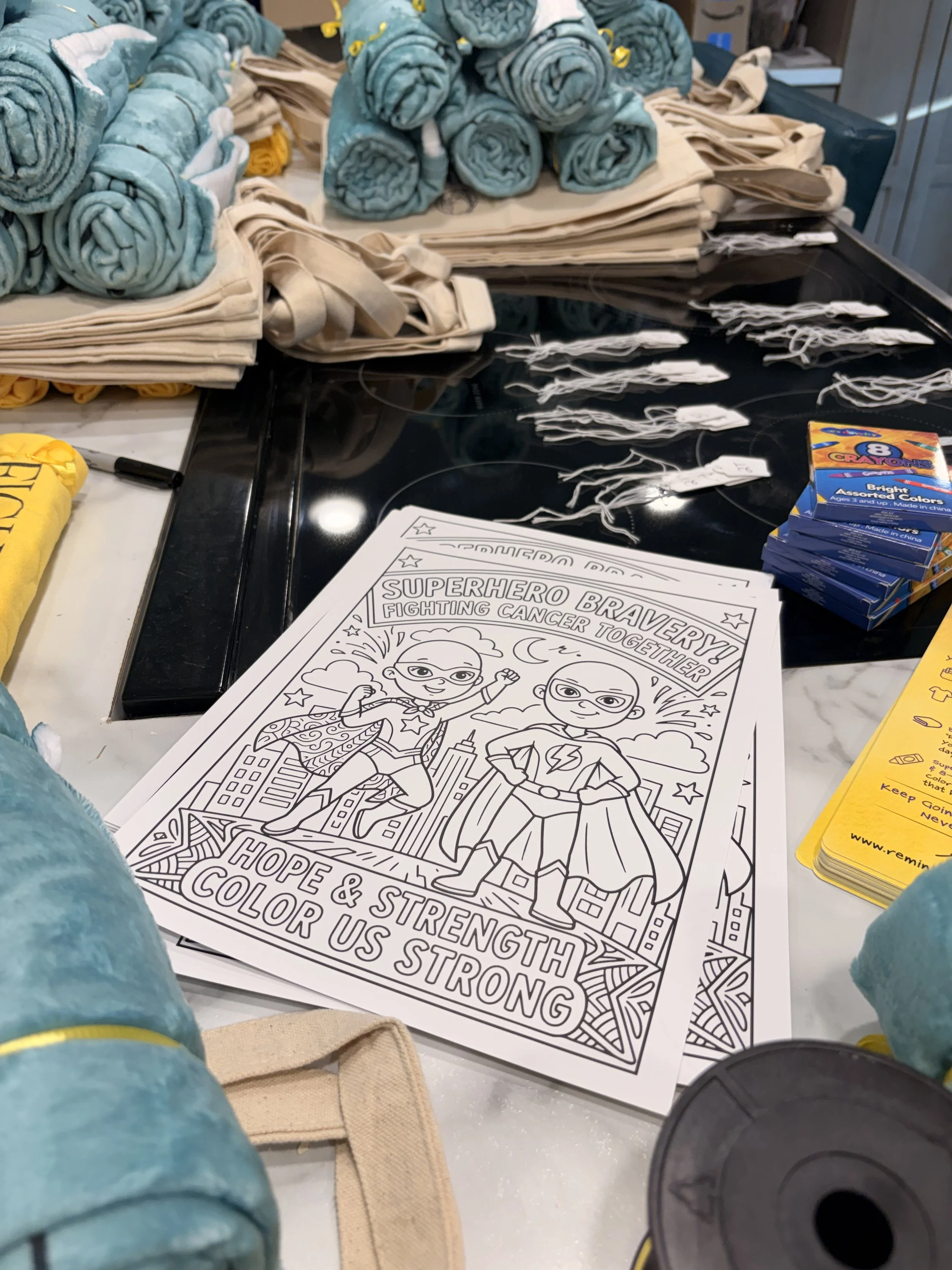 Superhero coloring page designed by Kim Survil, along with mindset gifts spread out for shirts, blankets, crayons and tote size tags.