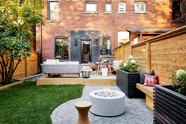 Outdoor backyard patio with seating, fire pit, and fencing in front of a brick building.