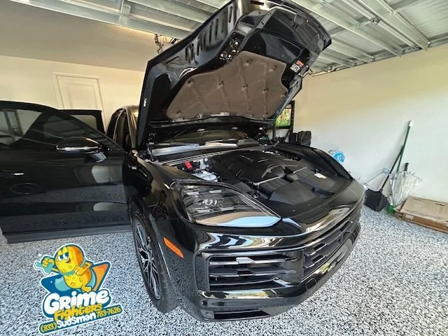 A black car with its hood open inside a garage, with a sticker on the floor that says 'Grime Fighters Washman'.