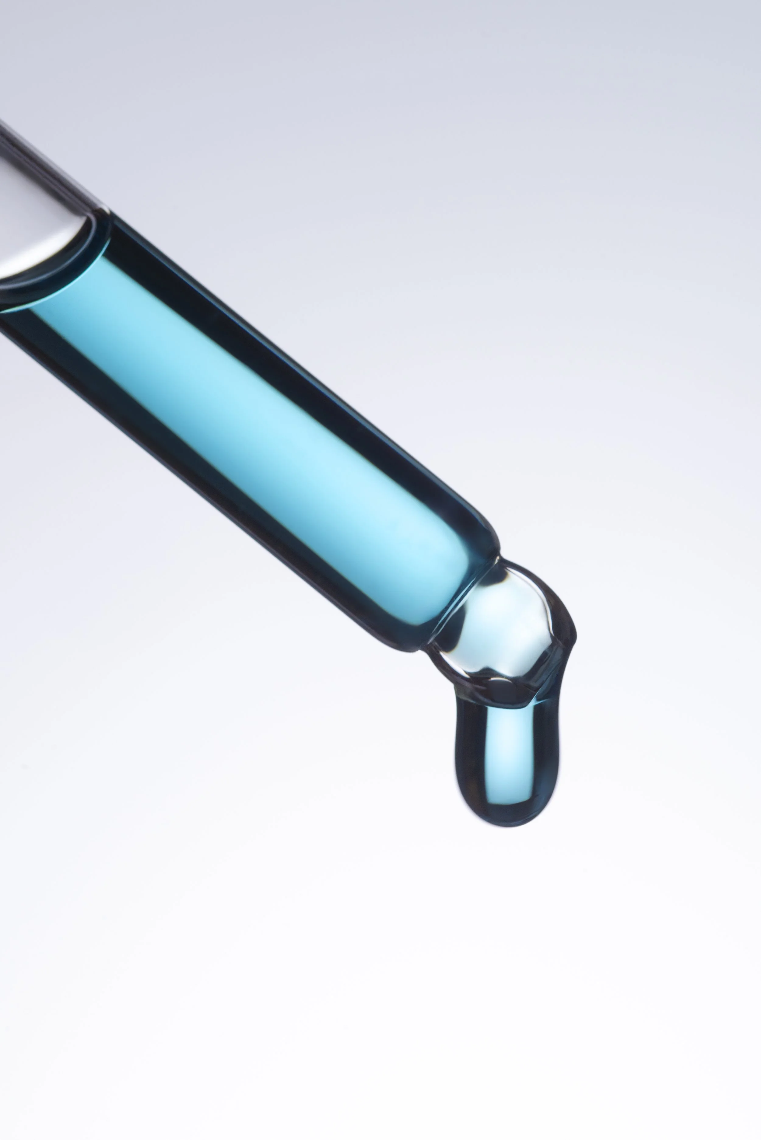 A close-up of a dropper releasing a blue liquid into a clear container.