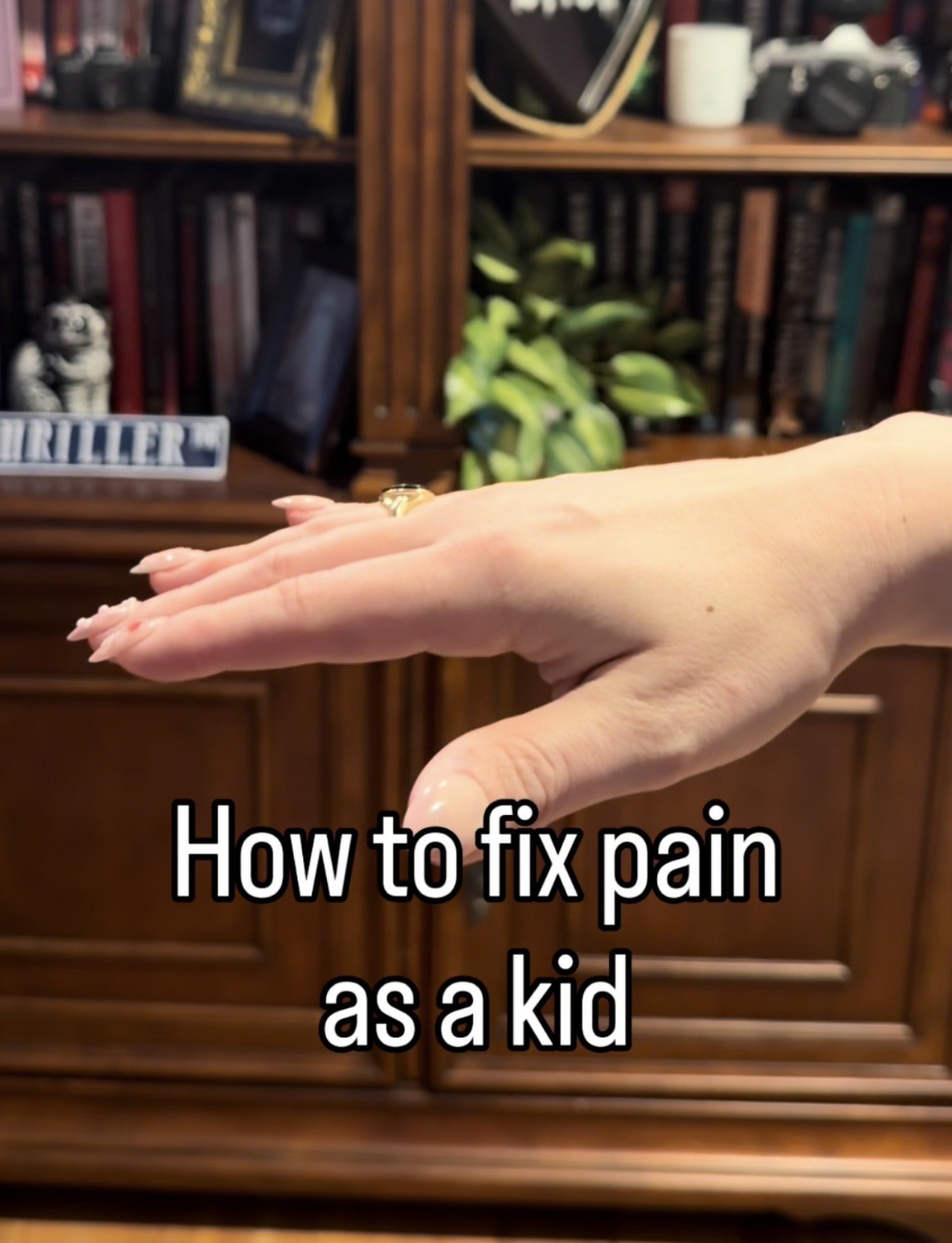 A hand with a ring on the finger extends in front of a wooden bookshelf with books and decorative items, with the text 'How to fix pain as a kid' overlaid.