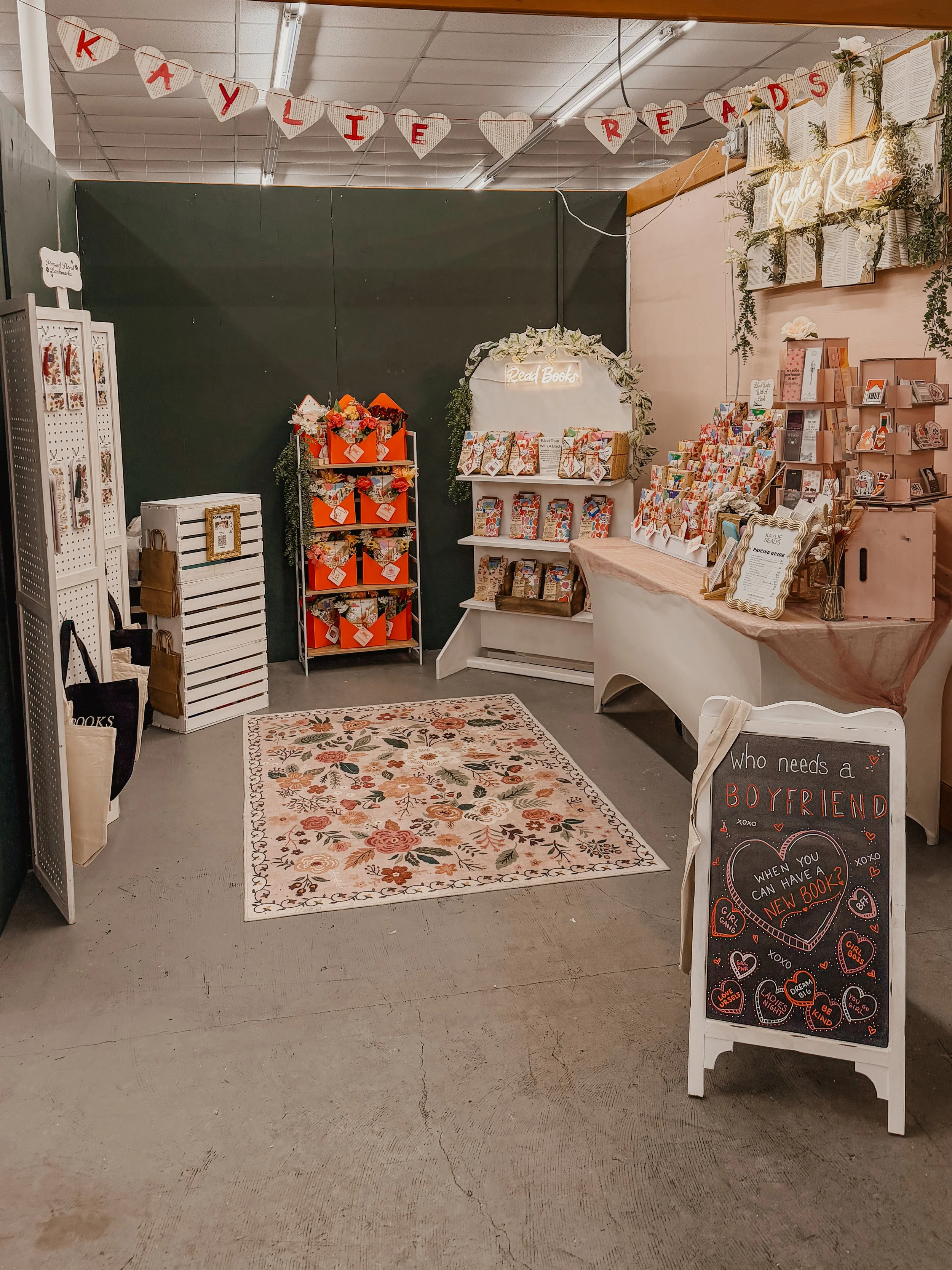 Valentine's Day themed display with love books, gift items, and decorative signs, including a banner reading 'Kaylie Reads' and a sign asking 'Who needs a boyfriend when you can have a new book?'
