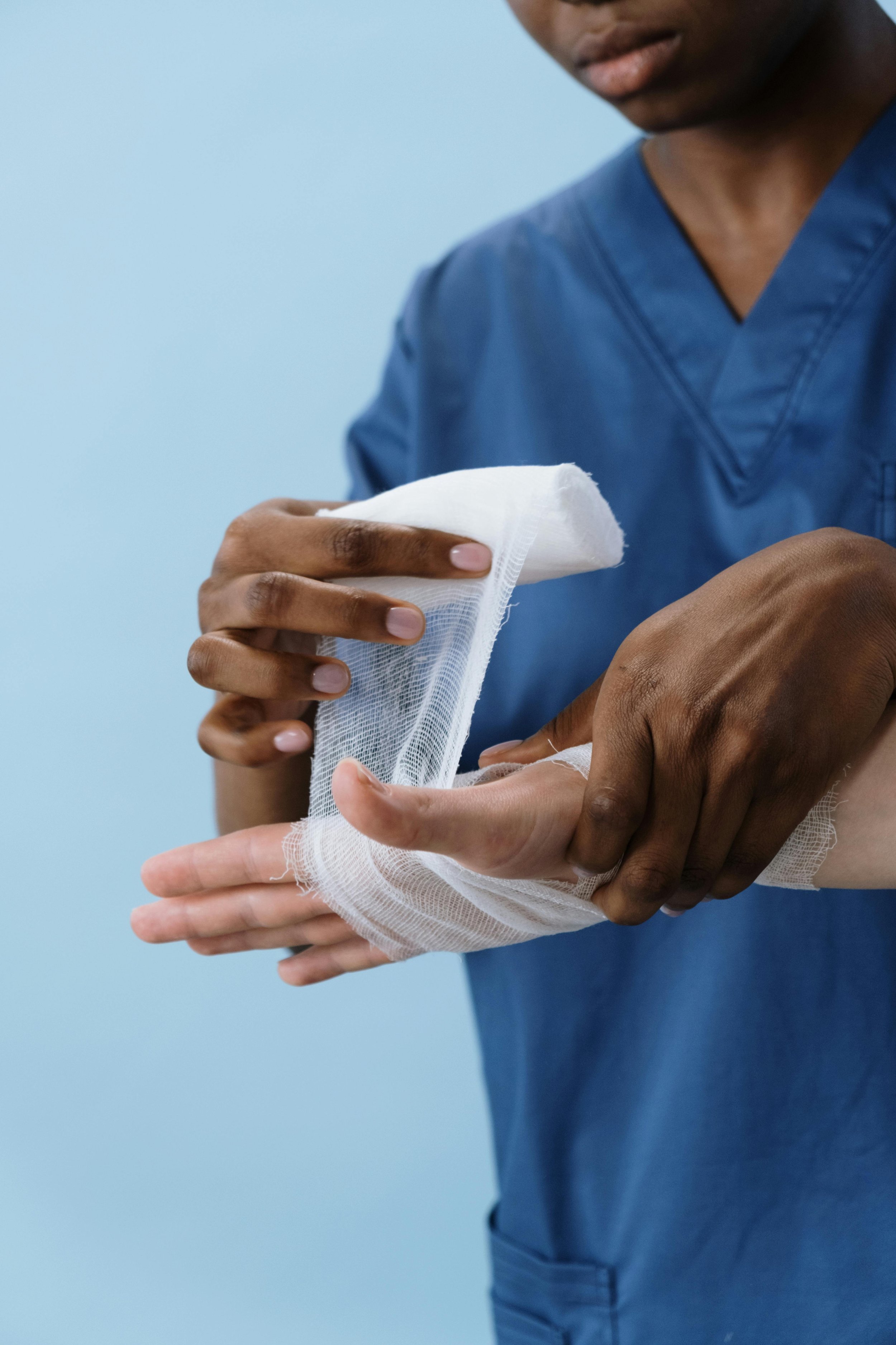 A medical professional in blue scrubs bandaging a hand