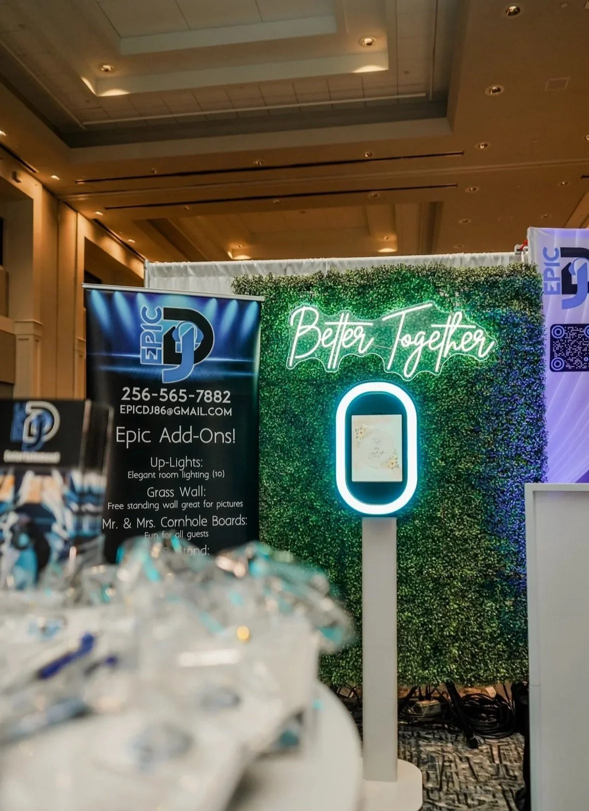 A neon sign that says 'Better Together' in front of a green and purple textured wall at an event, with promotional banners on either side promoting Epic DJ services.