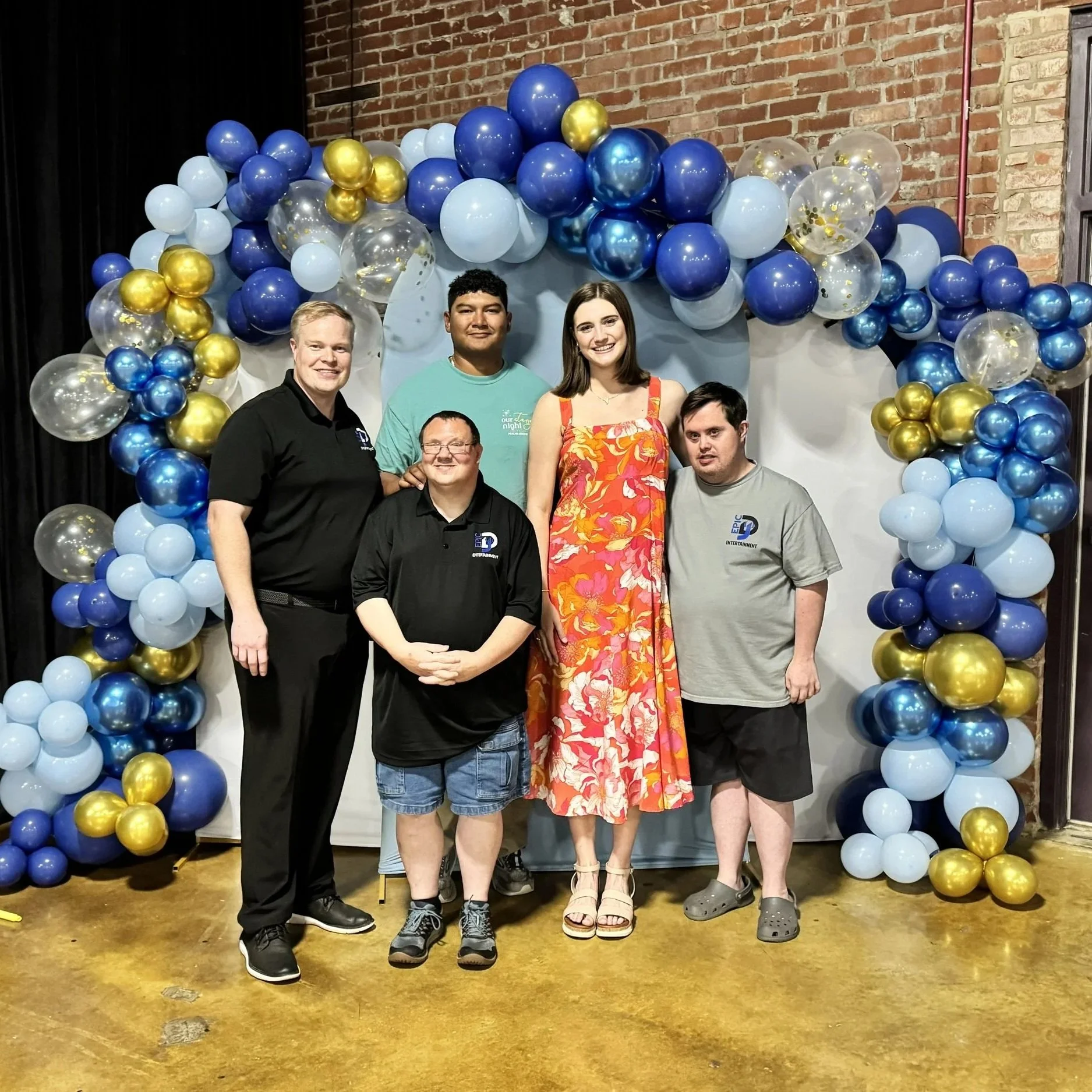 Five people standing in front of a balloon arch in a decorated indoor setting.
