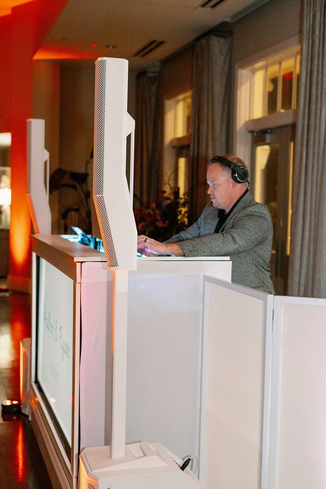 DD Drew standing at a DJ booth wearing headphones and playing music for a wedding party.