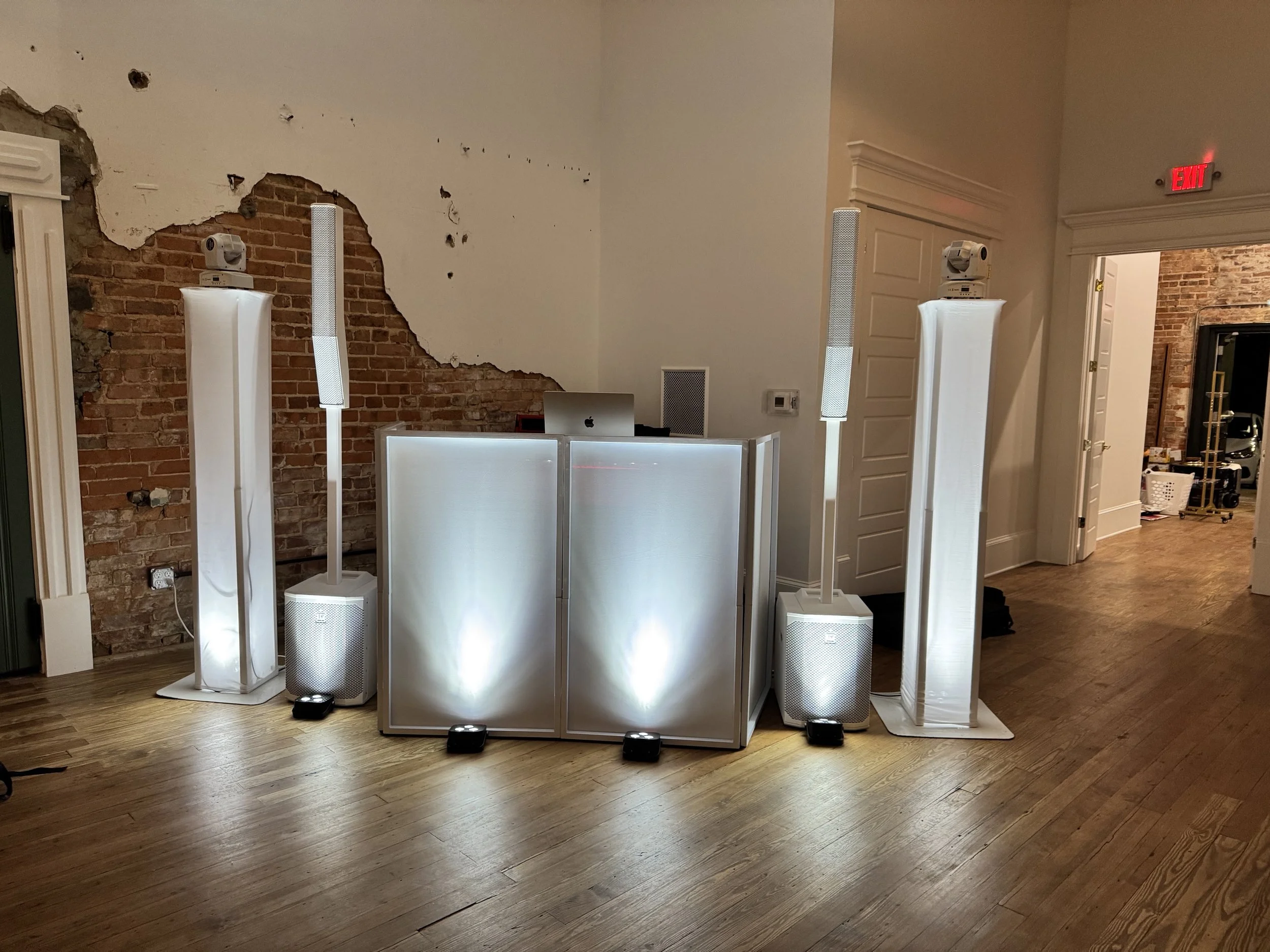A DJ setup with illuminated speakers and a mixer on a table, set up in a room.