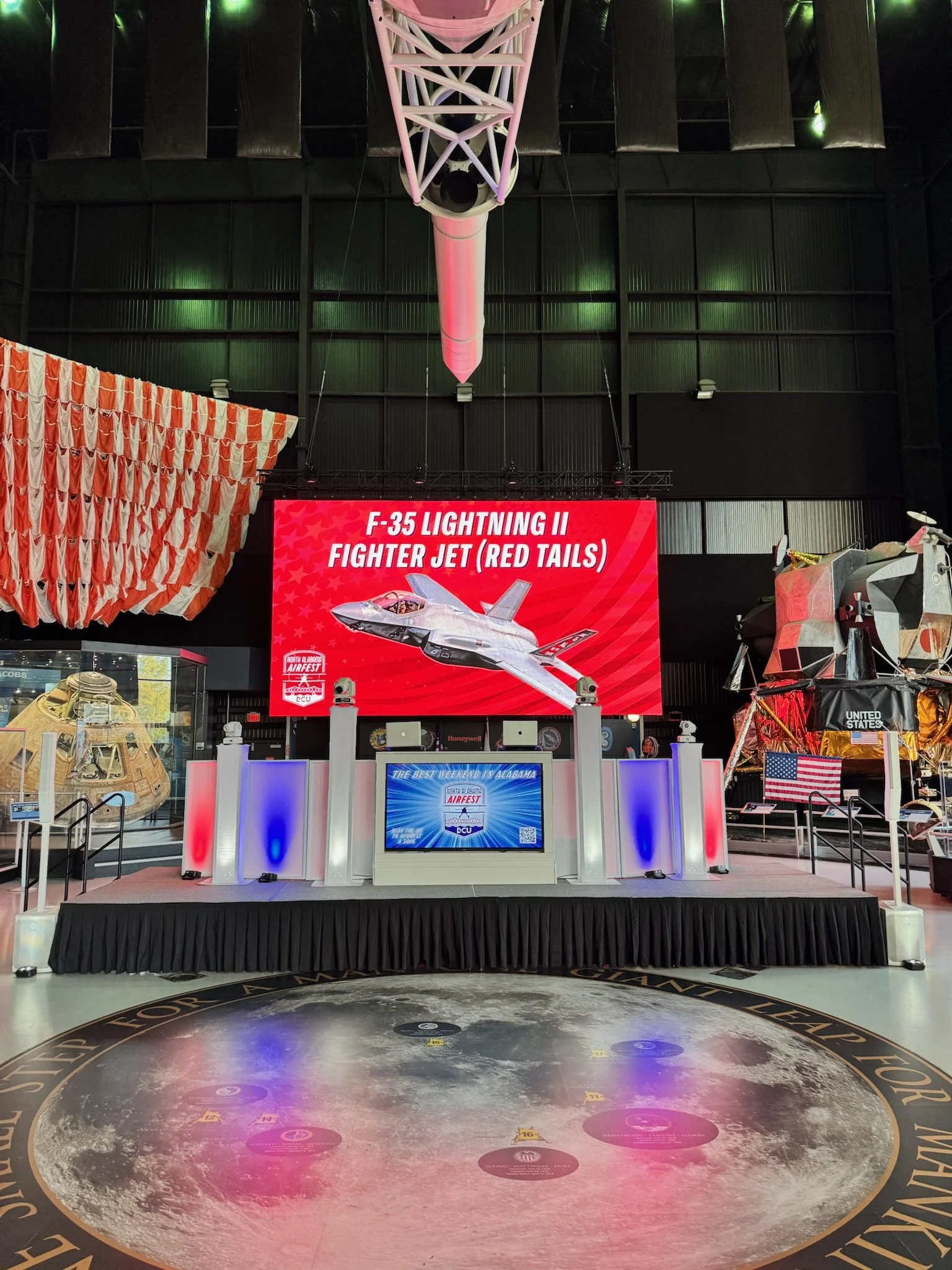 Exhibit at a space museum featuring a large digital display with a flight simulation of an F-35 Lightning II fighter jet, surrounded by space-themed decor and models of space capsules.