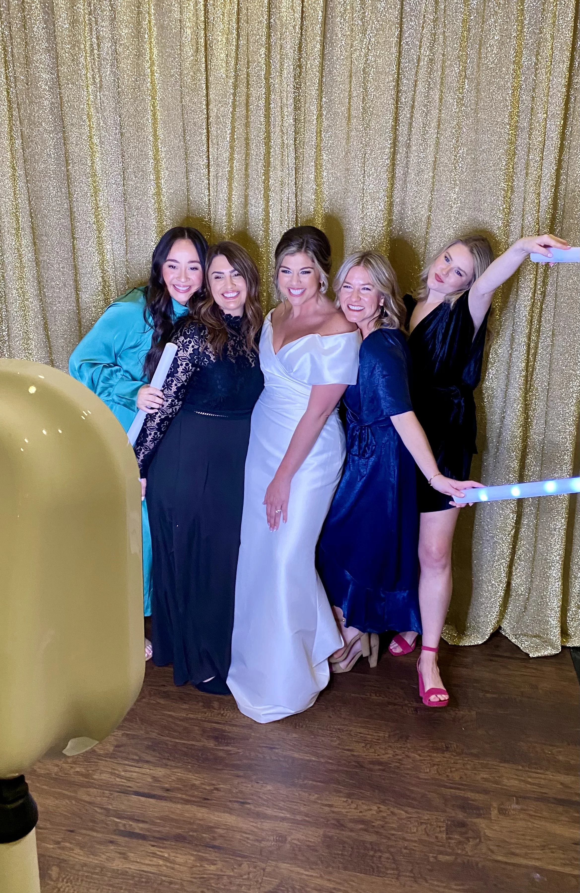 A group of five women posing for a photo in front of a gold glittery backdrop.