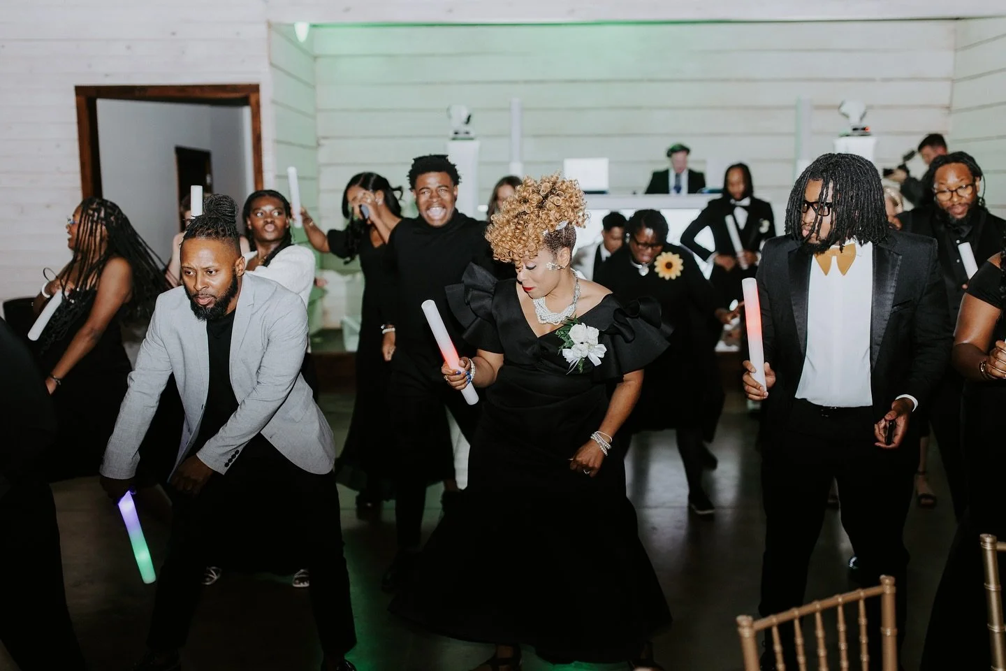 People dancing at a formal event, some holding glowing sticks, with a band playing in the background.