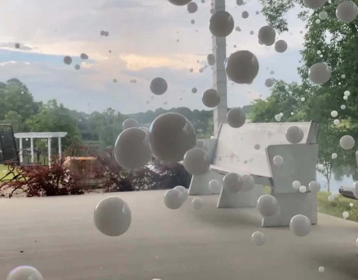 View of the front windshield of a vehicle with numerous small white and black spherical objects stuck on the glass, with an outdoor scene including trees, a statue, and a cloudy sky visible through the glass.