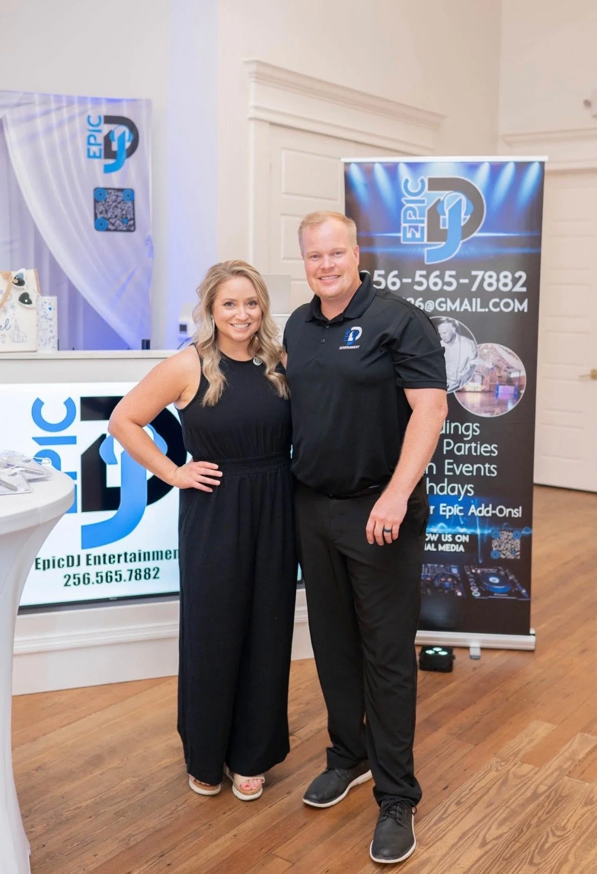 A man and woman standing together indoors, smiling at the camera, near promotional banners for Epic DJ Entertainment.