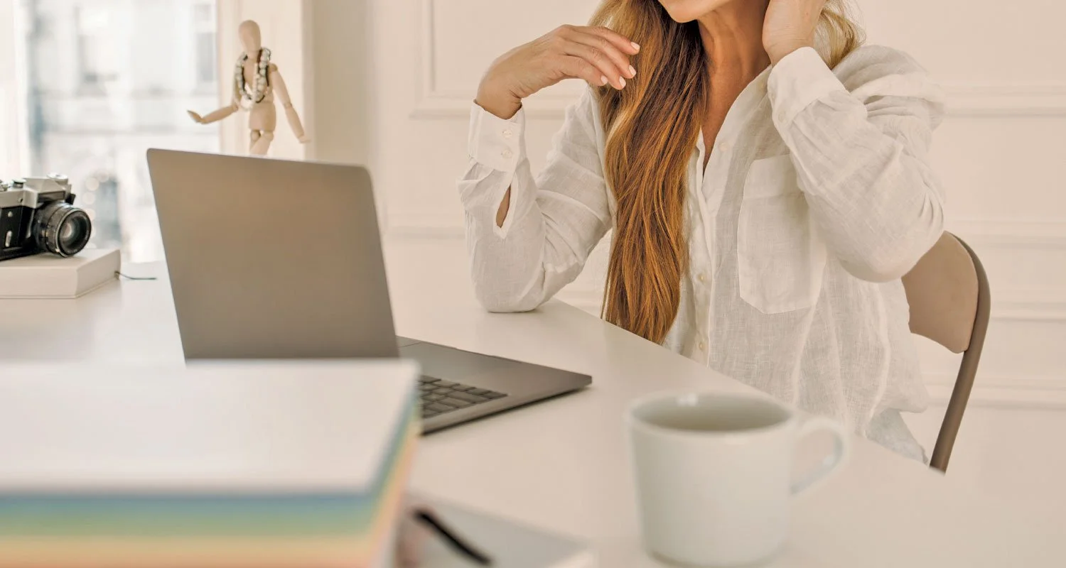 A woman sitting at her desk in front of her laptop with a mug of coffee.