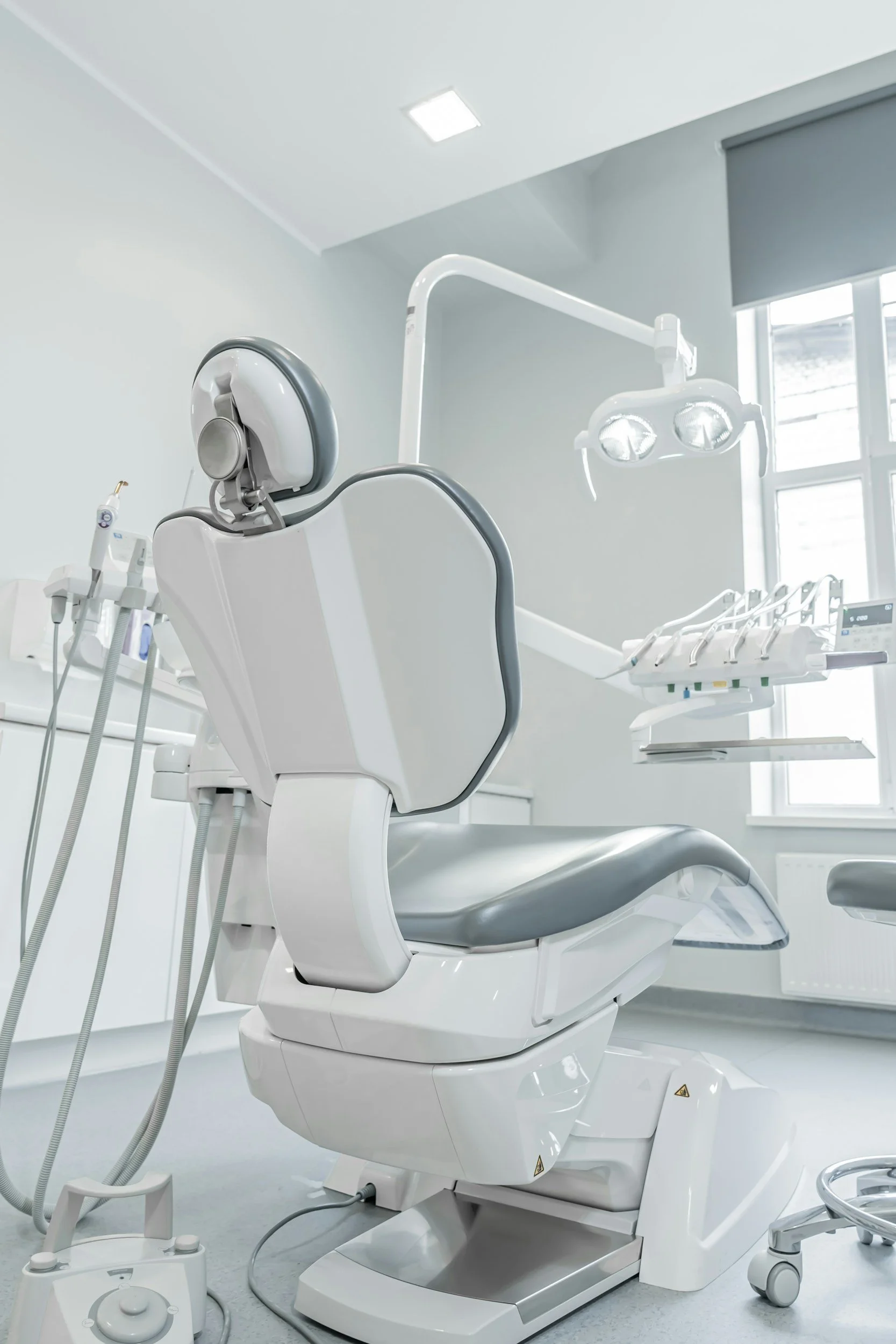 Empty dental examination chair in a modern dental clinic with overhead light and dental tools nearby.