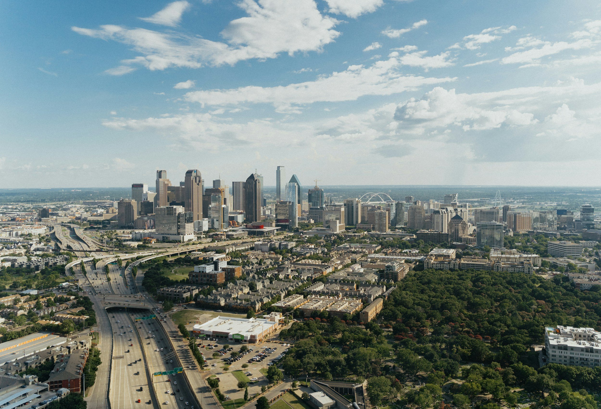 Aerial view of downtown Dallas, Texas with high-rise buildings, highways, and a partly cloudy sky.