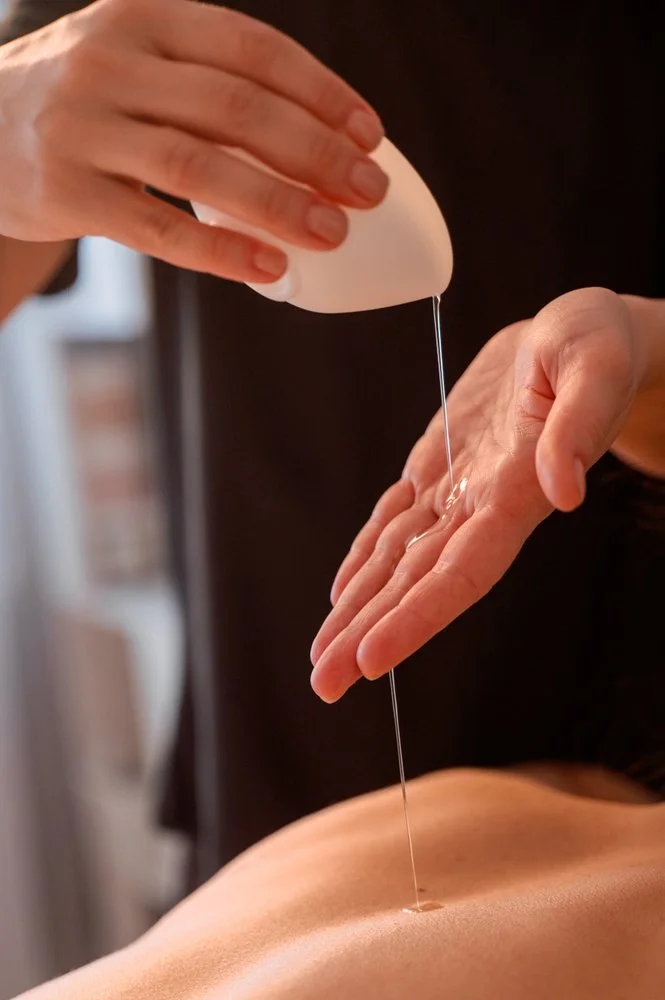 Massage therapist pouring warm massage oil onto a client’s back