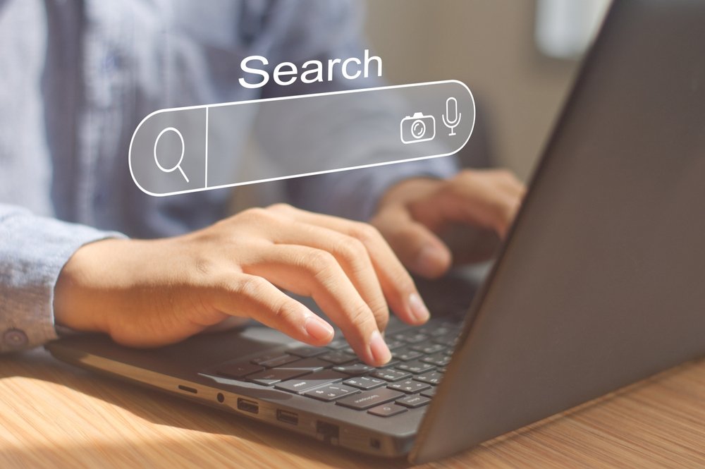 Hands typing on a laptop with a search bar overlay for online queries