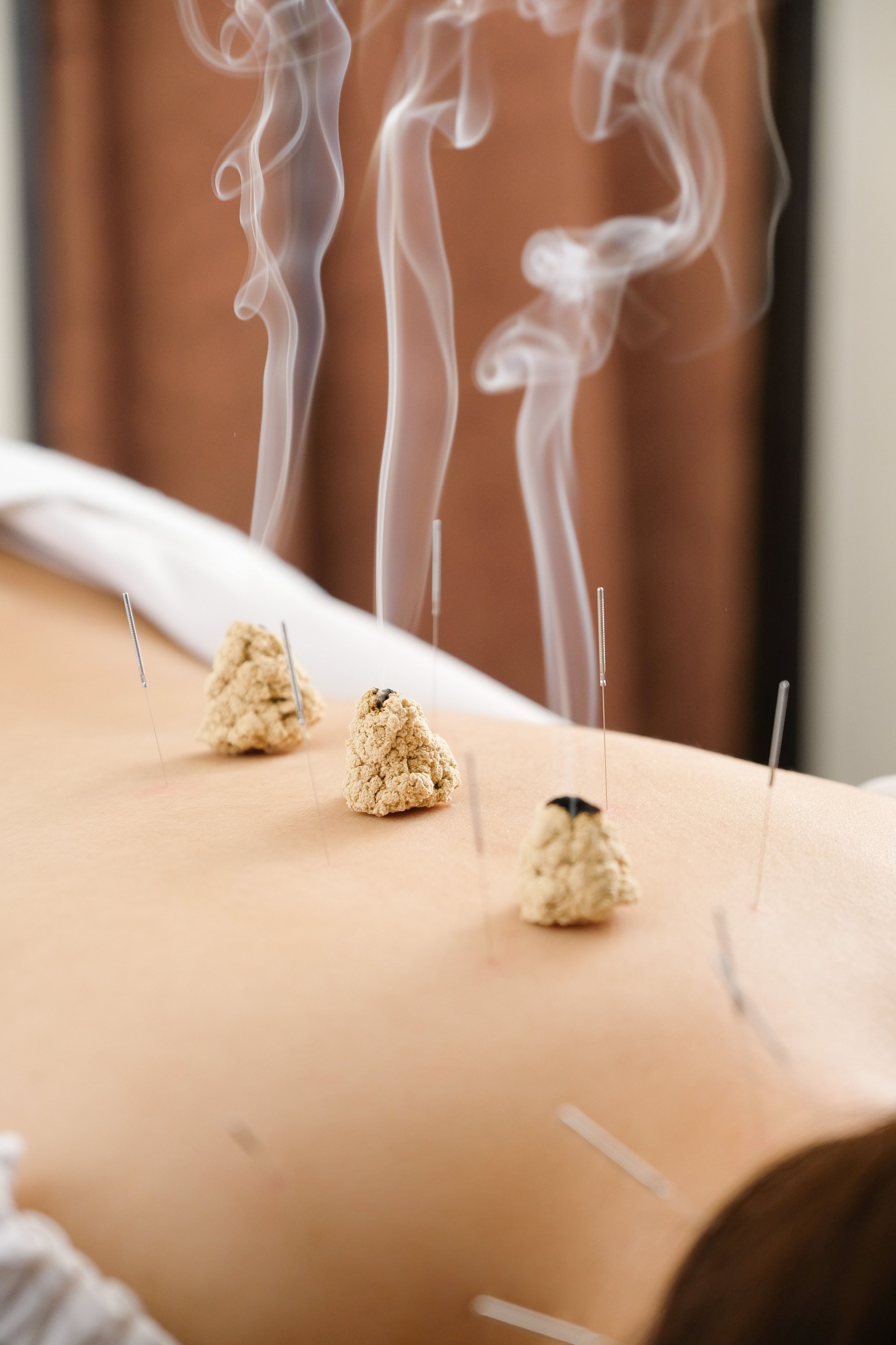 Several small pieces of edible paper with small bamboo sticks inserted, with incense sticks ignited and producing white smoke curling upward, placed on a wooden surface.