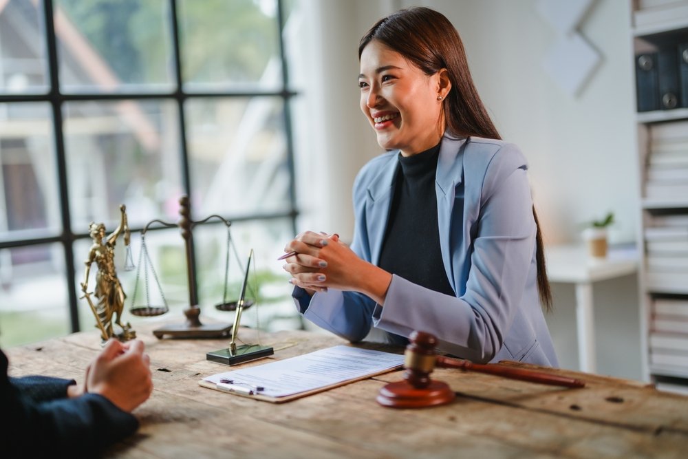 Lawyer smiling while consulting a client at a desk with legal documents.
