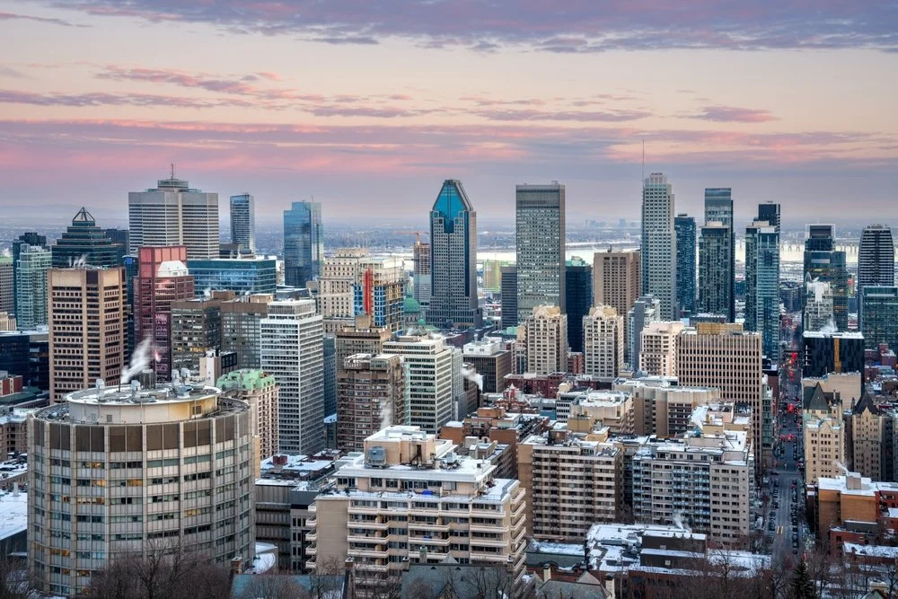 Urban skyline at sunset with snow-covered rooftops and high-rise buildings.