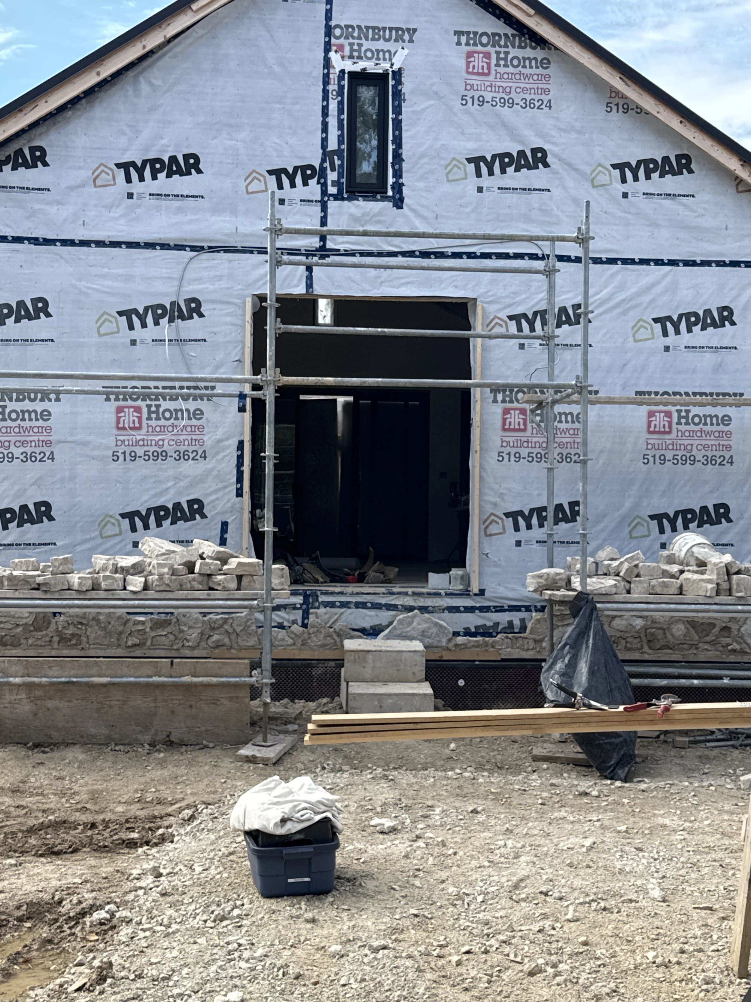 Front of a house under construction with scaffolding, bricks, and construction materials in front.