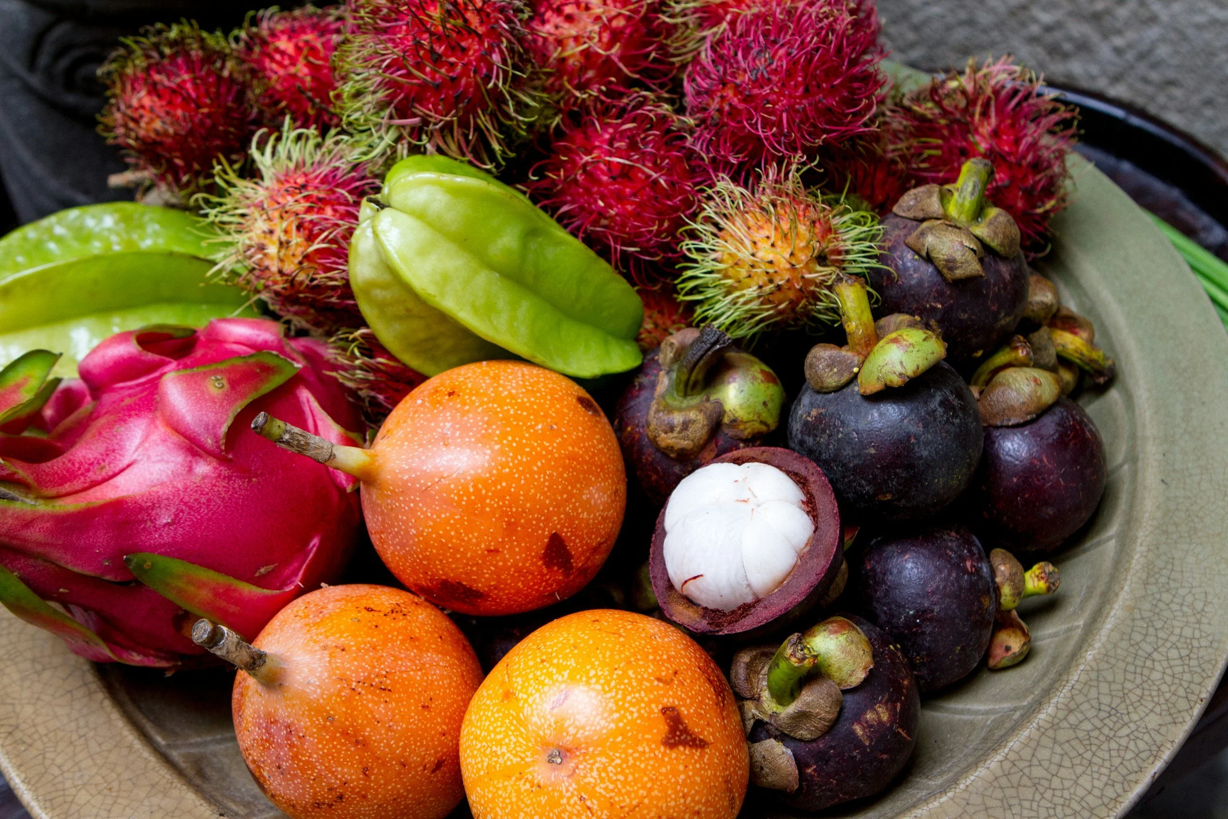 A plate of various tropical fruits including dragon fruit, starfruit, oranges, mangosteen, and rambutan.