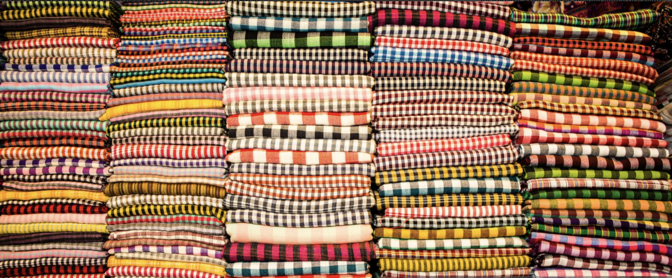 Stacks of folded checkered and plaid fabric in various colors, arranged on shelves.