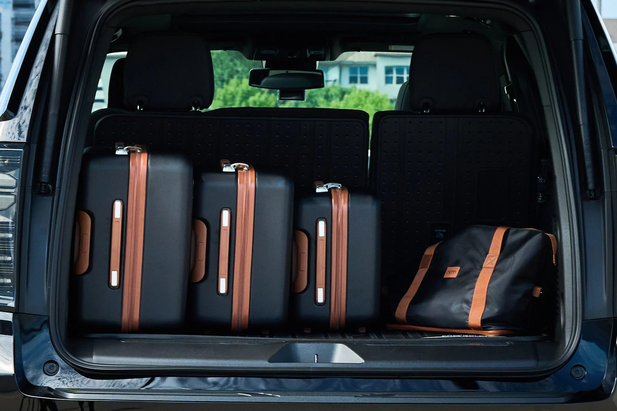 The trunk of a car with four black suitcases and a black bag with brown handles and accents.
