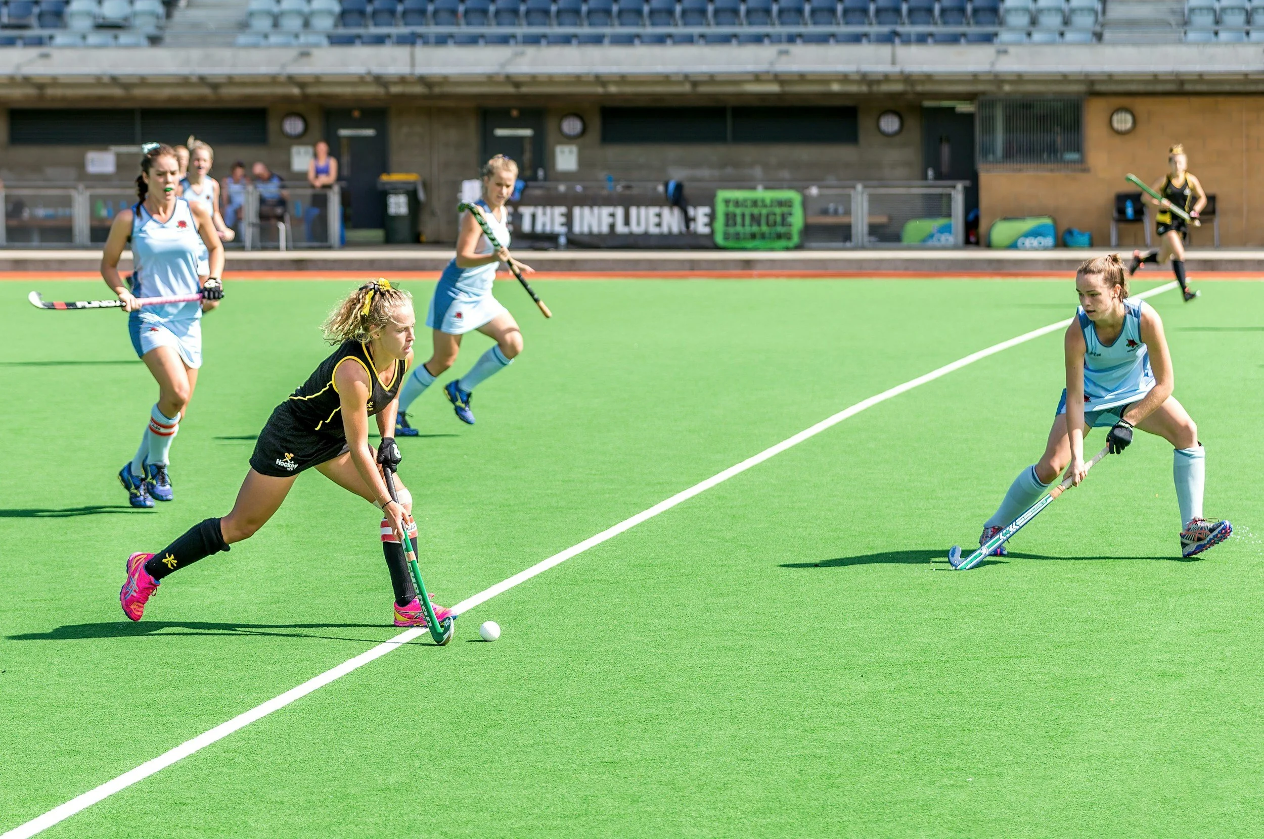 Girls playing field hockey on a bright green turf field during a game.