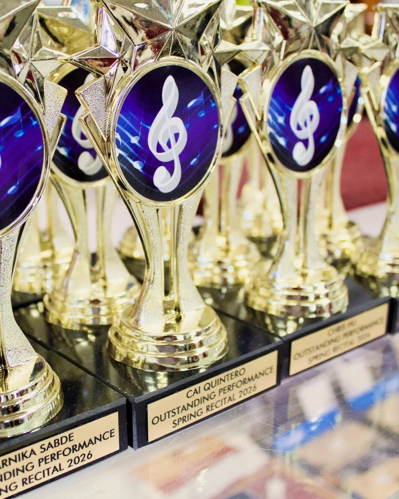Close-up of gold trophies with a circular emblem featuring a white musical note and background with digital music notes, displayed on a black shelf with labels for various award categories.