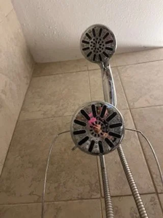 Showerhead with two connected nozzles mounted on a tiled wall in a bathroom.