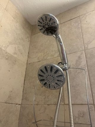 Showerhead and handheld shower attachment in a shower with beige tile walls.