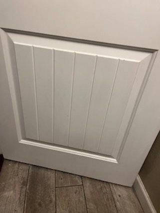 Close-up of a white door with vertical paneling, set in a room with laminate wood flooring.