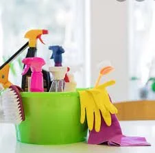 Cleaning supplies in a green container, including spray bottles, rubber gloves, and a cleaning cloth, on a countertop.