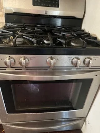 Stainless steel gas stove with four burners and oven, in a kitchen.