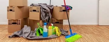 Unassembled cardboard boxes, cleaning supplies, and cleaning tools in a room with hardwood floors