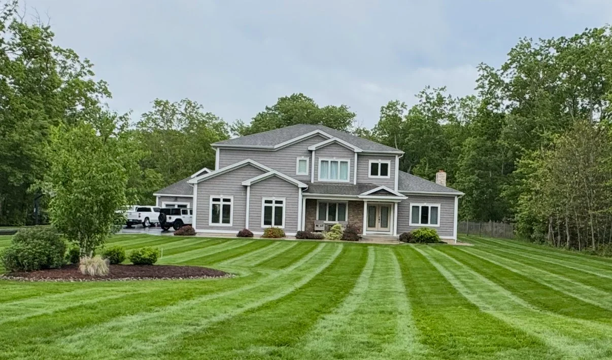 Modern gray two-story house with a well-maintained green lawn and trees in the background.