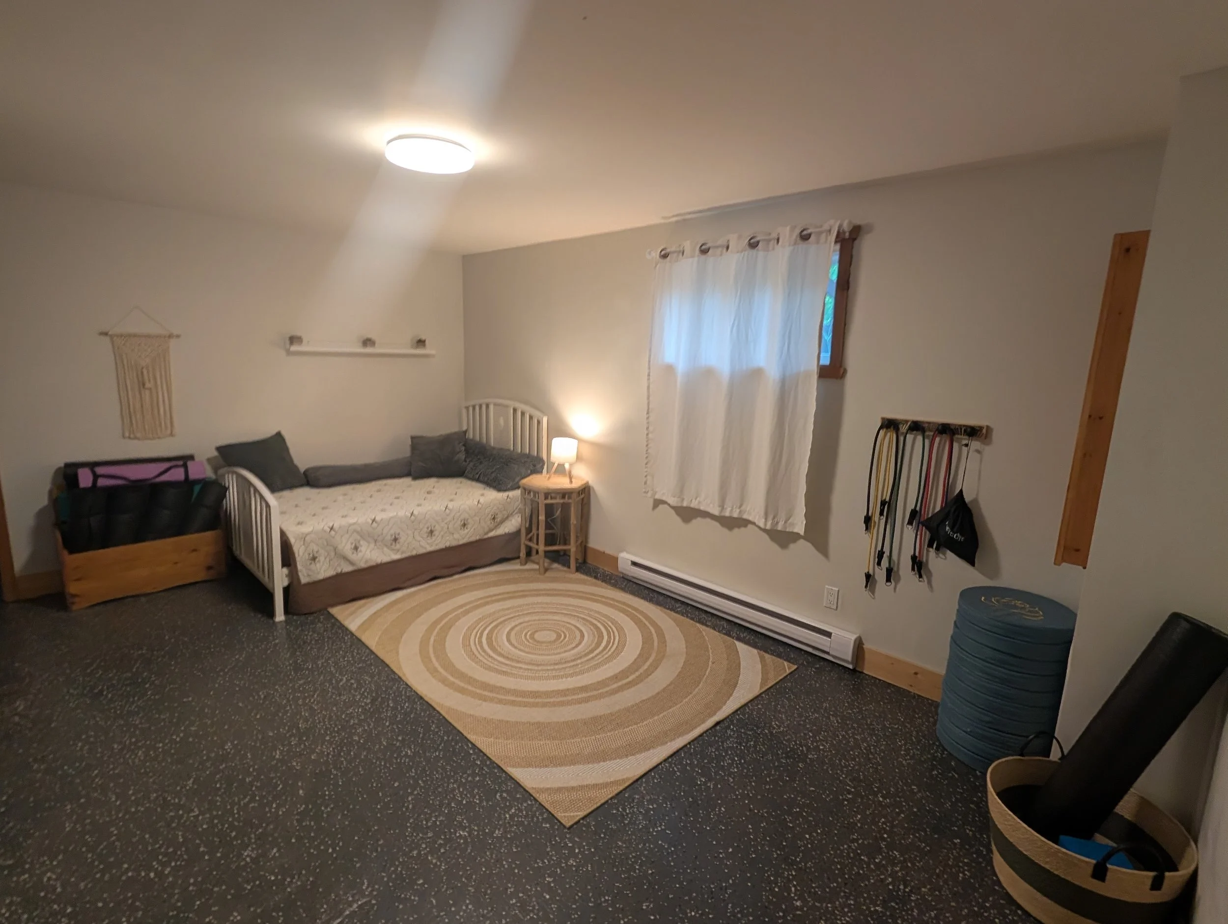 This lower-level open-concept space includes a dbl bed and yoga/exercise area. Please note this is not a private room — there is no door, and the space is open to the lower level.