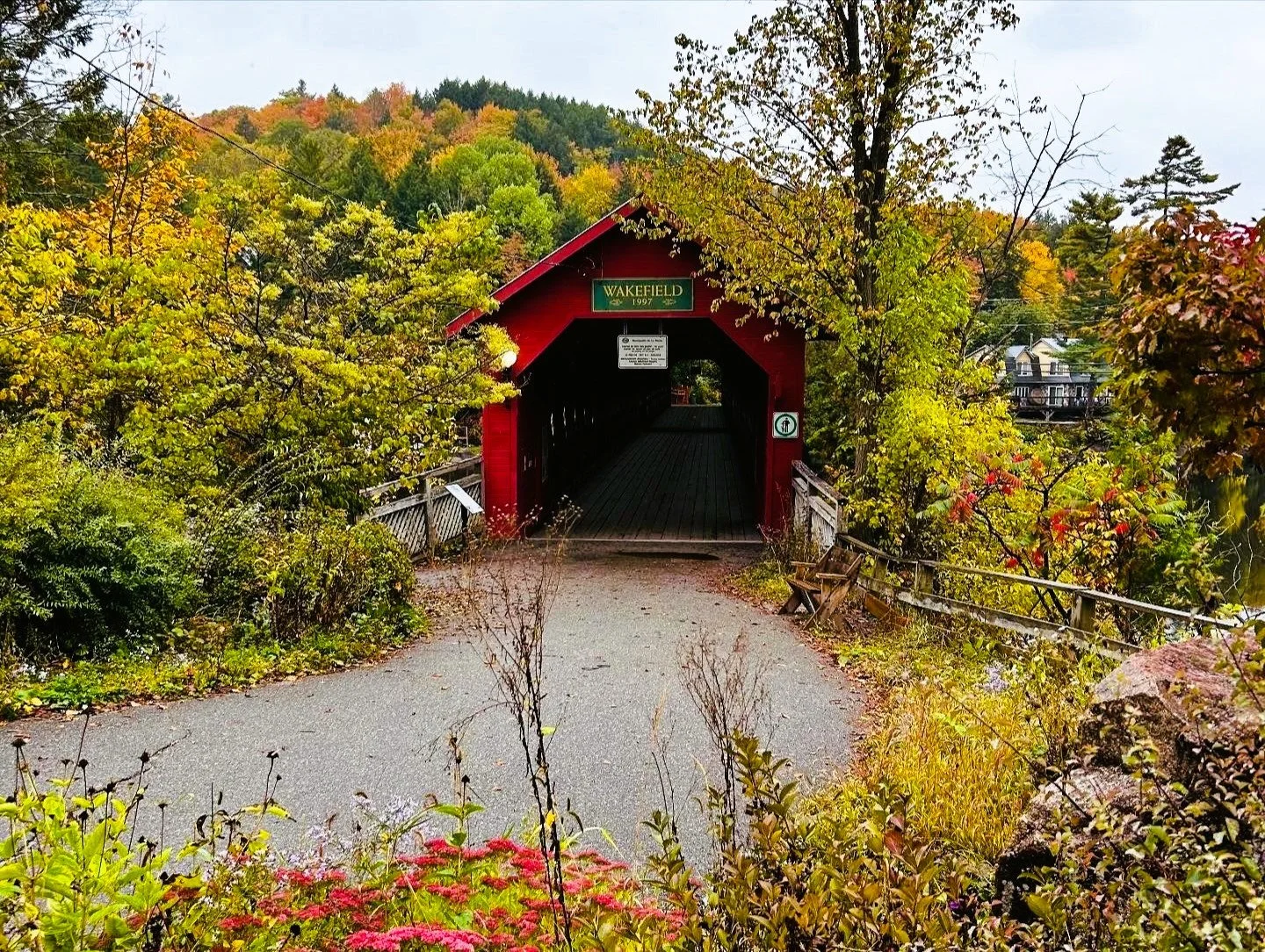 A small covered bridge in a park, surrounded by autumn foliage.