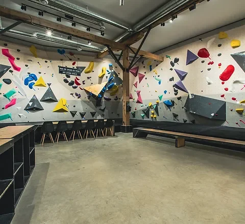 Indoor bouldering gym with various colorful climbing holds on the walls and seating area along the walls.
