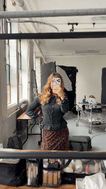 A woman taking a mirror selfie in a room with large windows.