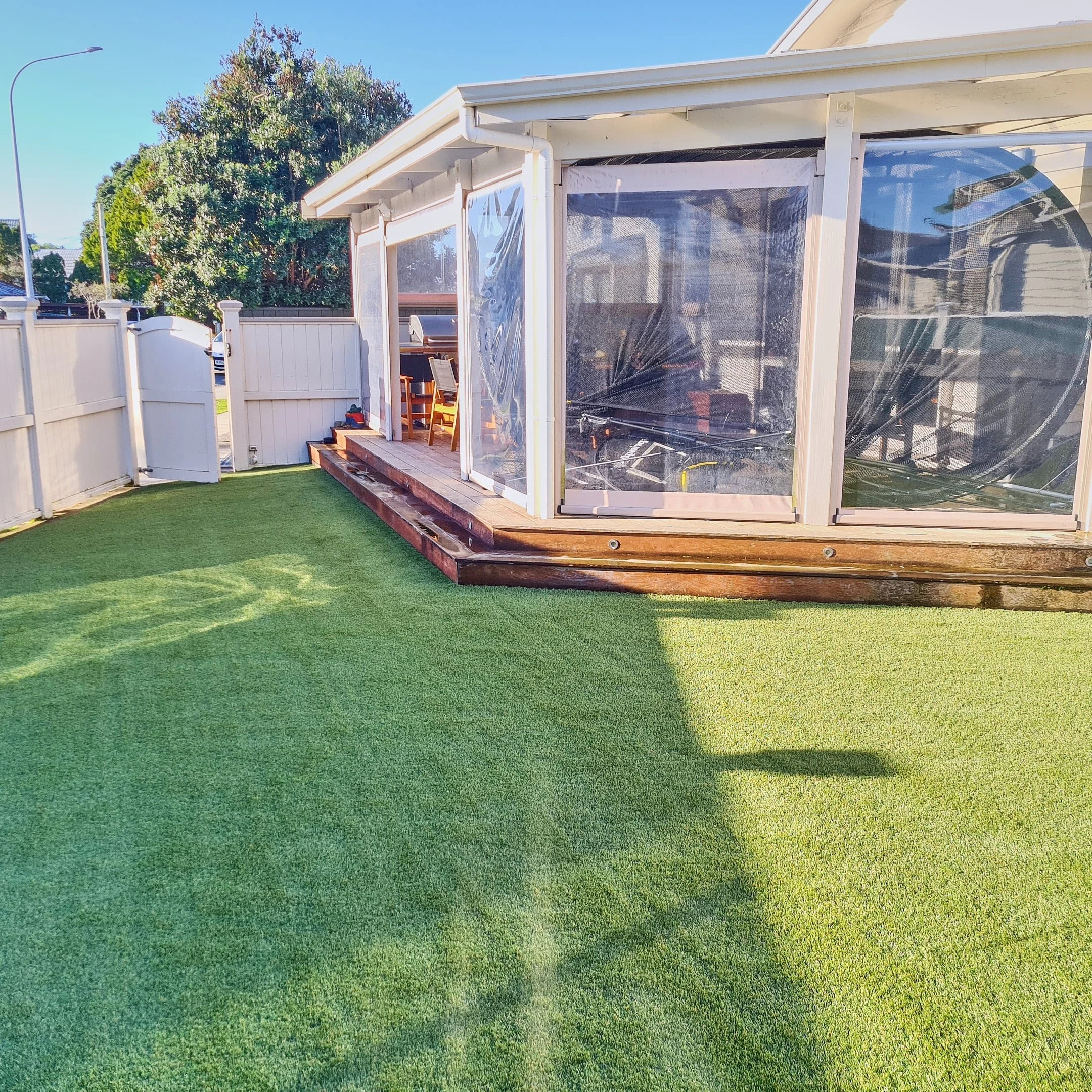 Backyard with artificial grass, a white fence, and a screened patio with outdoor furniture.