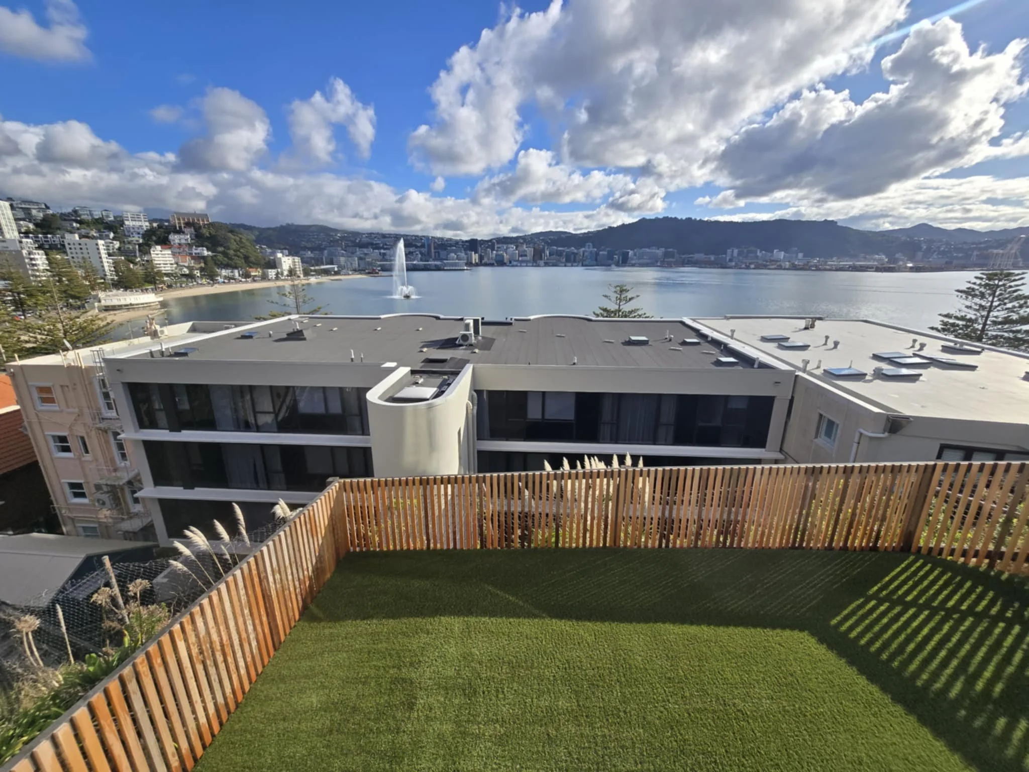 View from a balcony overlooking Wellington, New Zealand cityscape, water, and a fountain on a partly cloudy day in Oriental Bay.