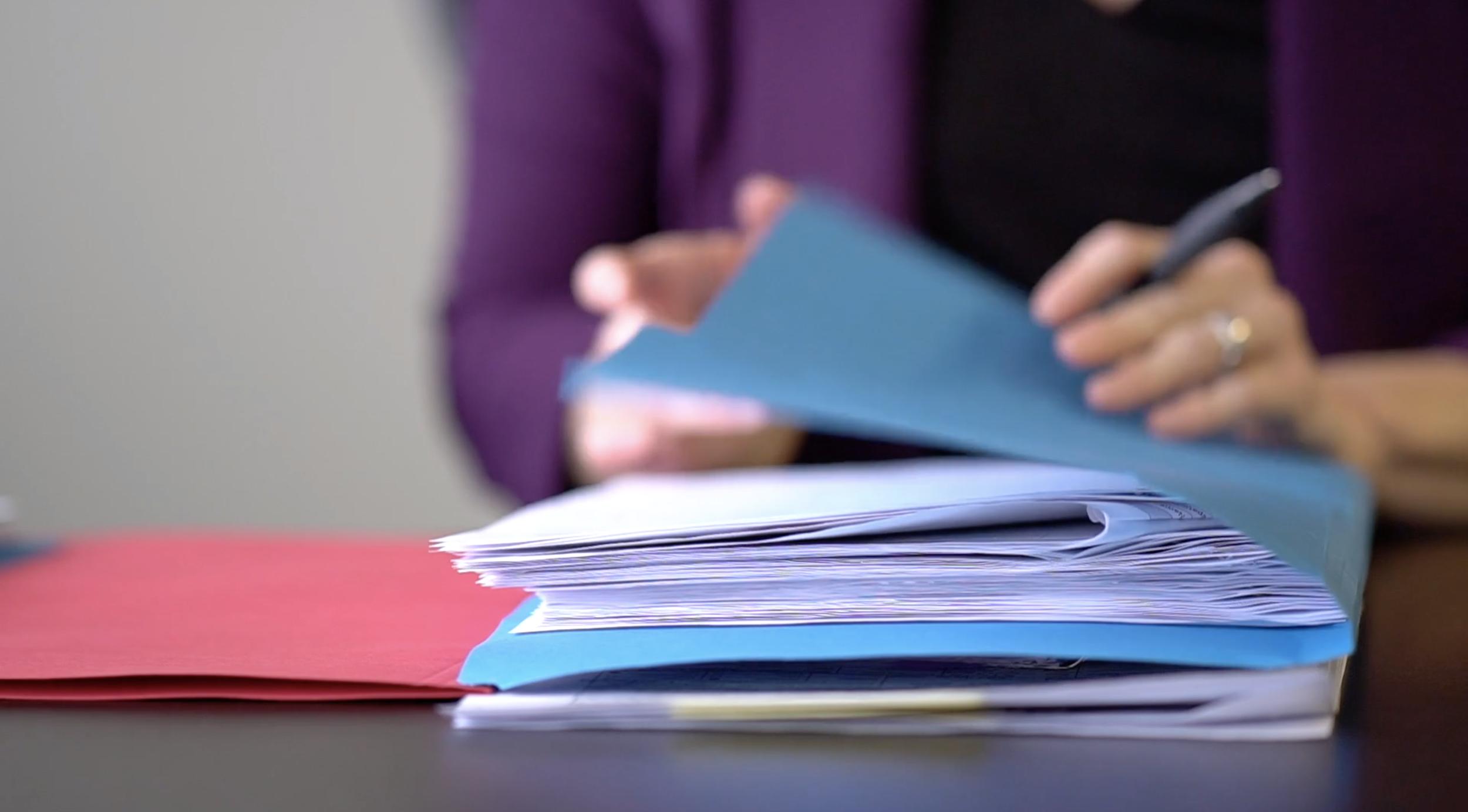 Close-up of a person writing or stacking papers and files, with colorful folders on a desk.