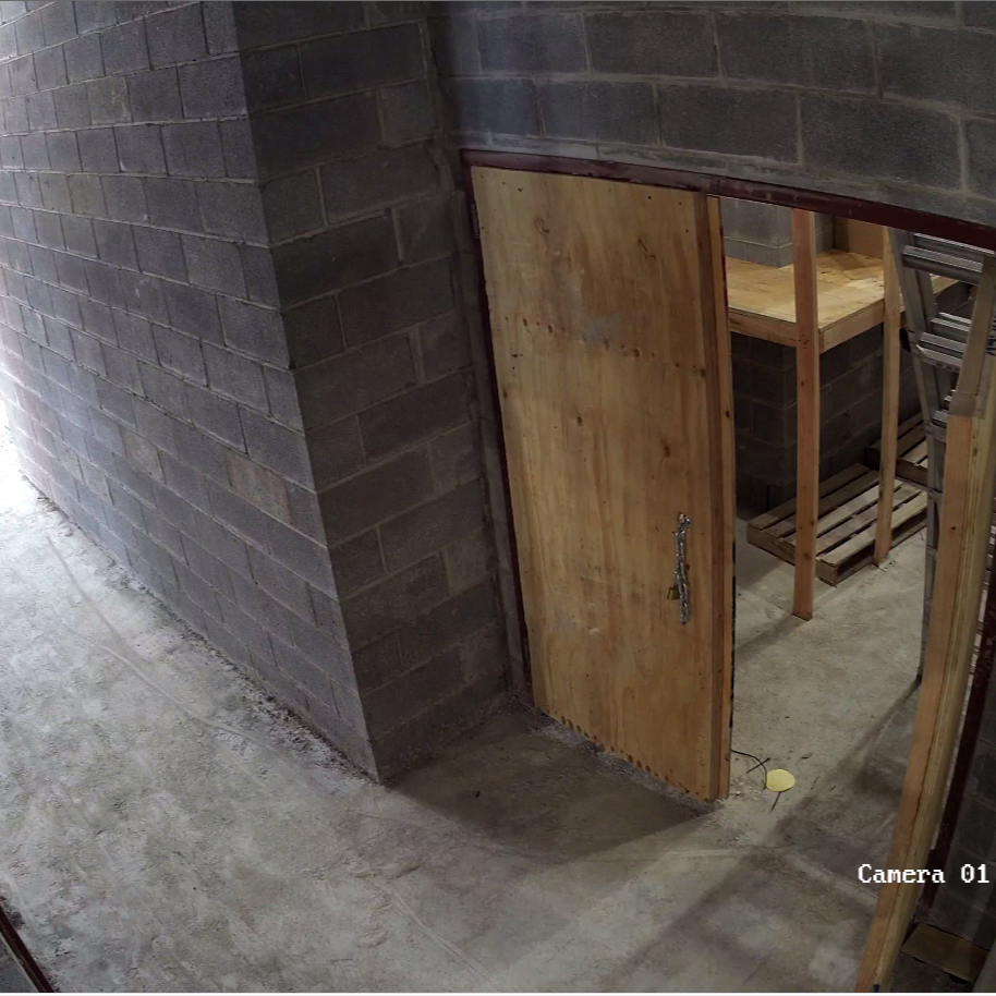 Construction site with a partially open wooden door leading into a room with unfinished wooden framing and a ladder.
