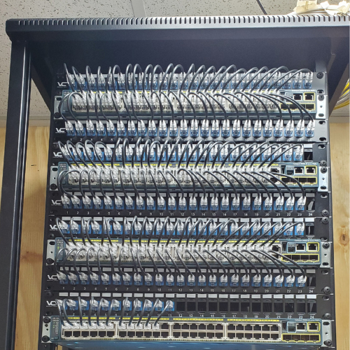 A network rack with multiple row of interconnected network switches and patch panels with numerous Ethernet cables connected.