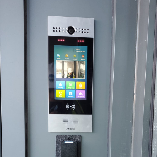 Digital security or access control panel mounted on a wall, featuring a screen displaying options and a camera at the top.