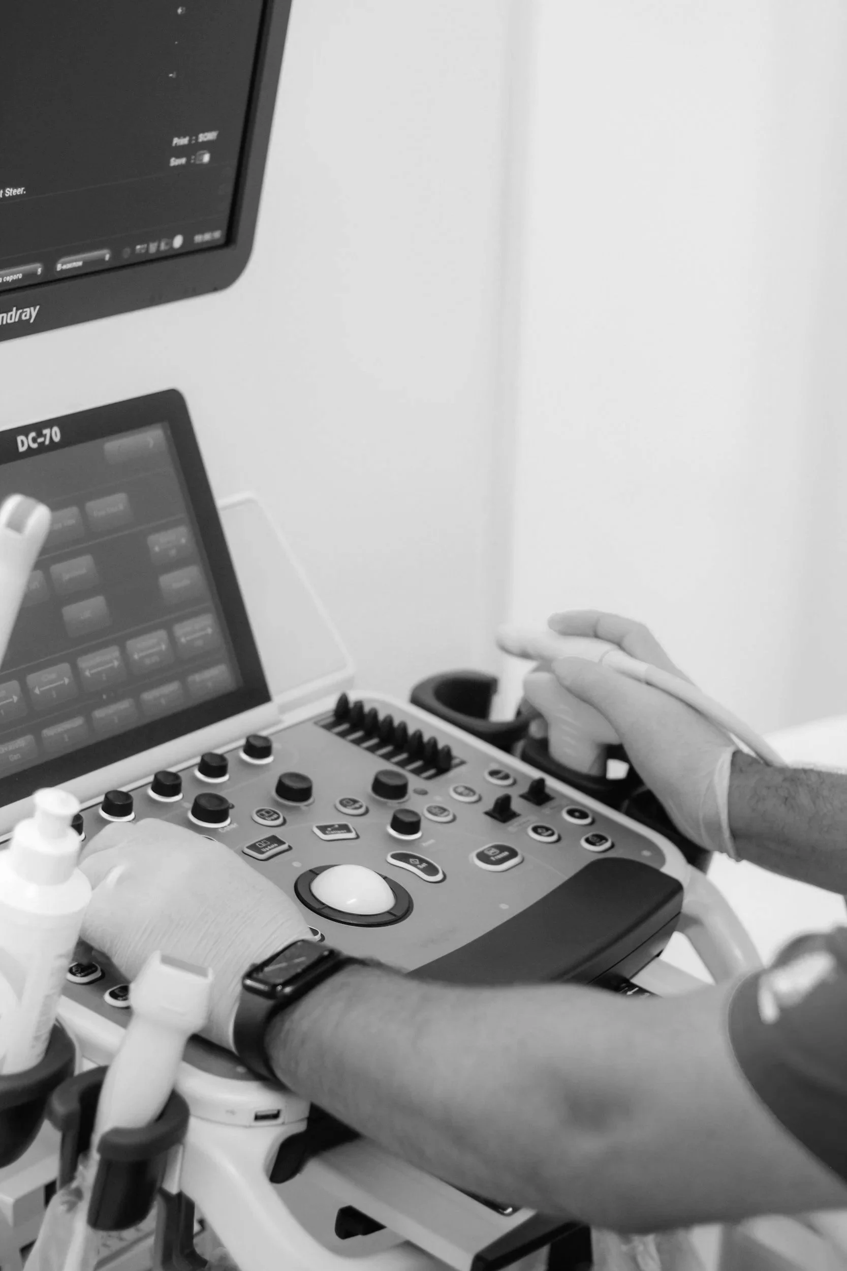 Medical professional wearing gloves operating ultrasound or medical imaging device in a clinical setting.