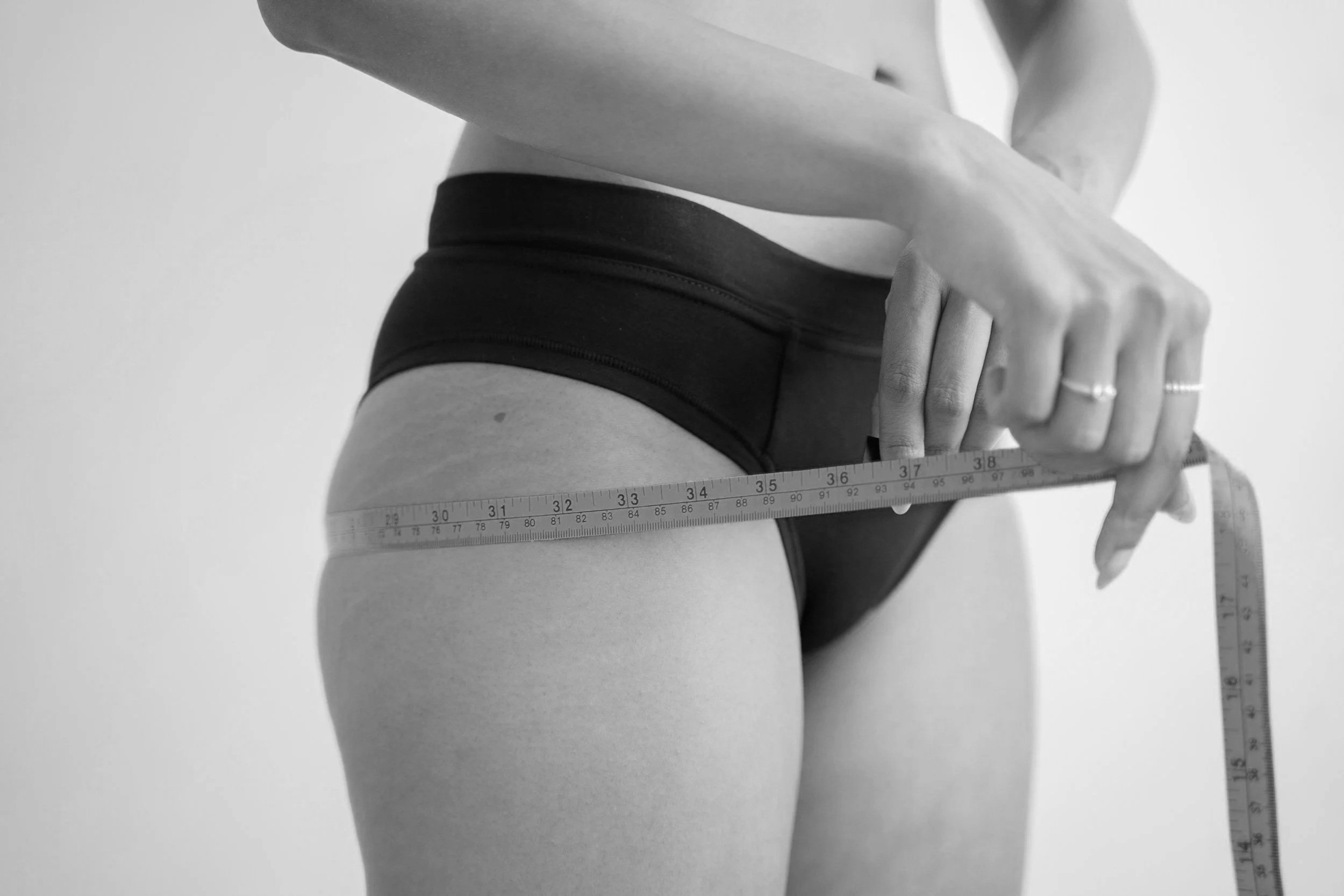 A person in black underwear measuring their waist with a ruler.