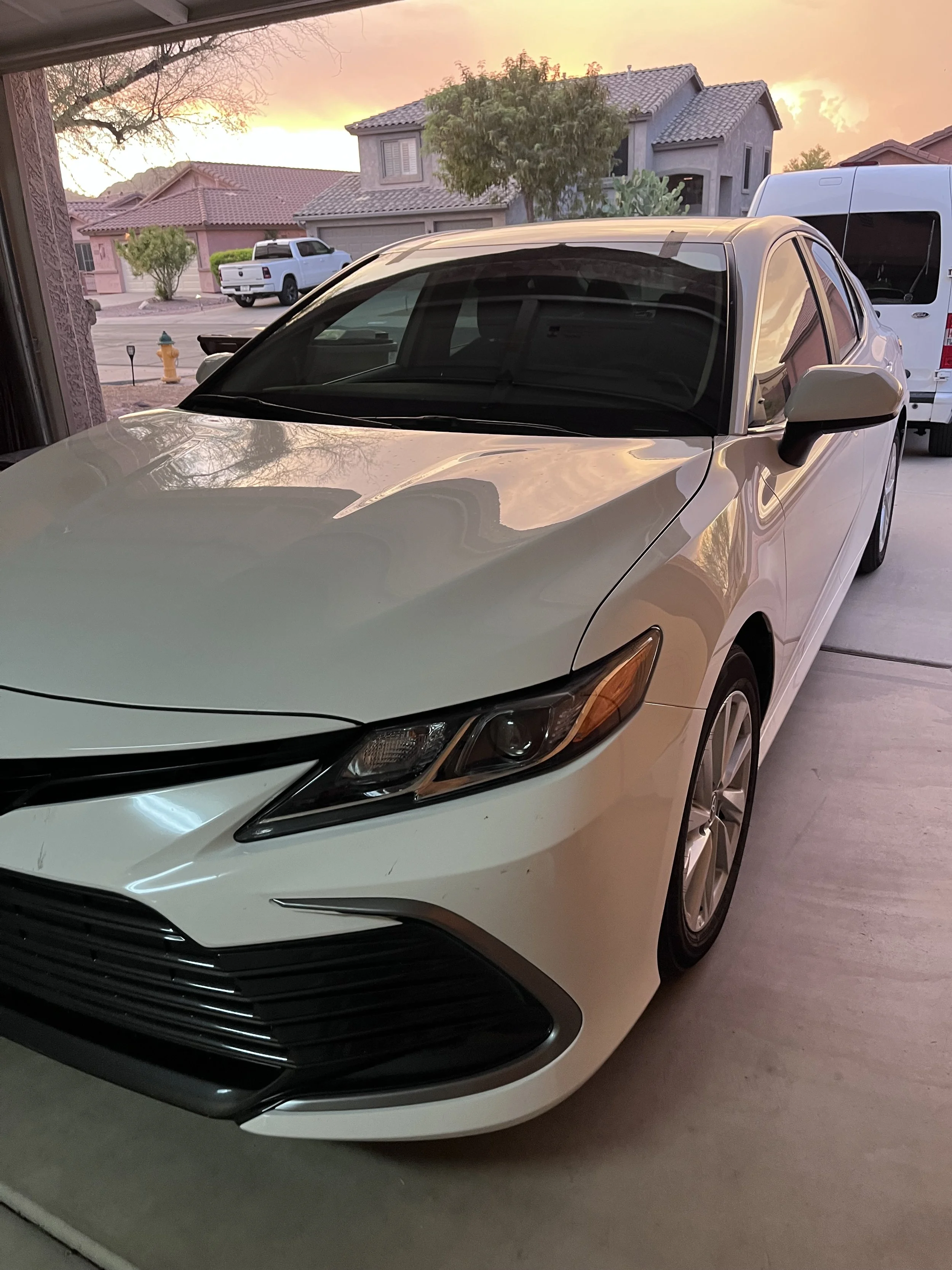 A white sedan parked in a garage during sunset, with houses and trees visible outside.